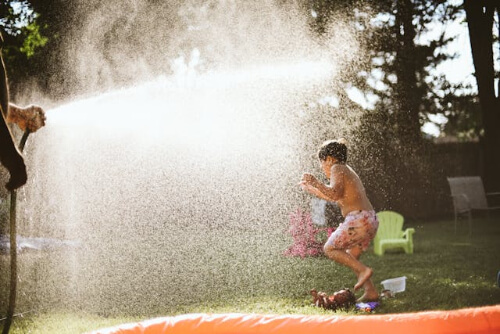 Boy running through water sprinkler
