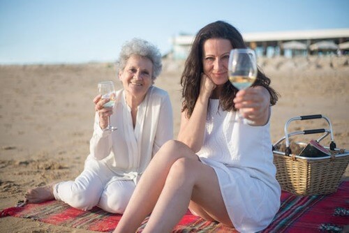 Daughter and mom sitting on the beach drinking wine. 