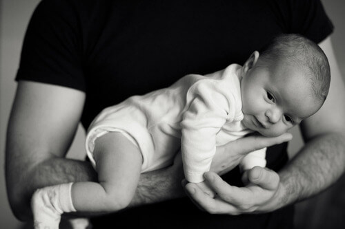 Dad cradling infant in arm.