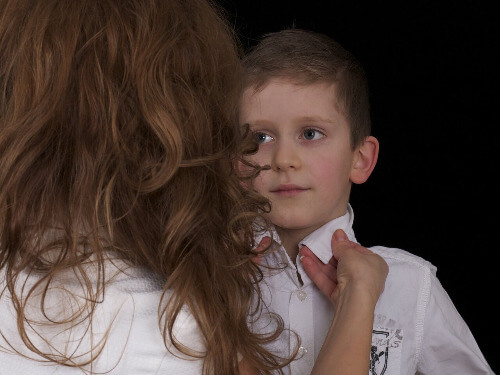 Boy looking at mom while she is tying tie.