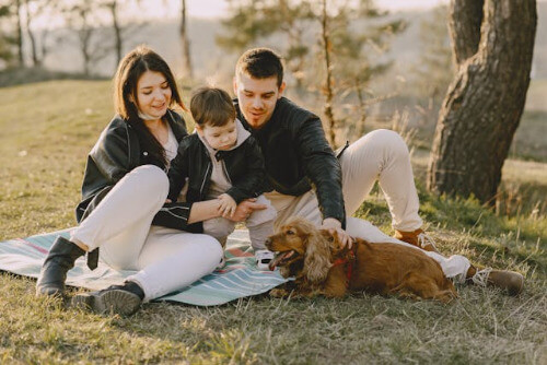 Family sitting outside by tree with dog.