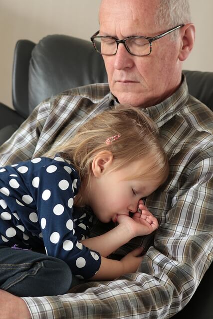 Granddad sleeping with granddaughter on his knee. 