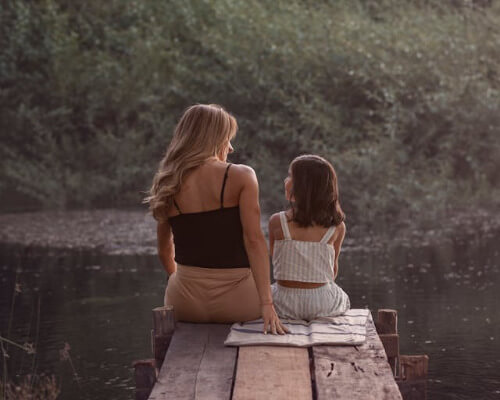 Mom and daughter sitting at the end of a dock communicating.