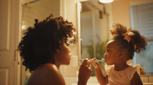 Mom helping toddler brush teeth.