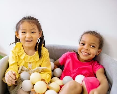 two preschoolers in a small container of balls
