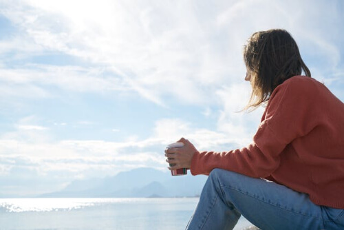 Woman sitting on the beach while drinking a coffee.