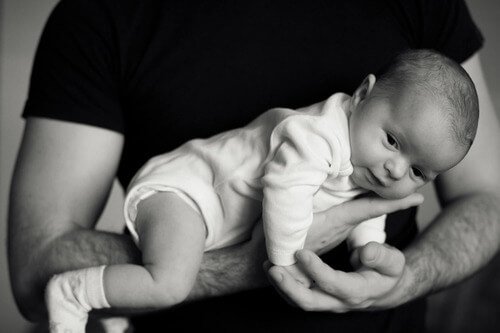 Dad cradling infant in arm.