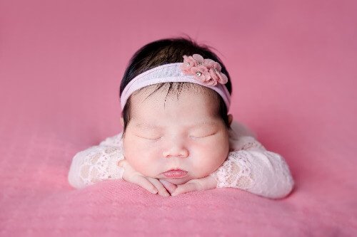 New born bsby girl on her tummy with arms under her head.