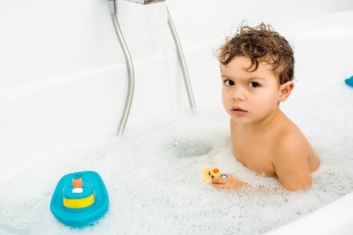Toddler in bubble bath with boat.