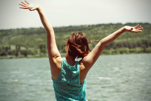Woman throwing her arms in the air while facing lake 